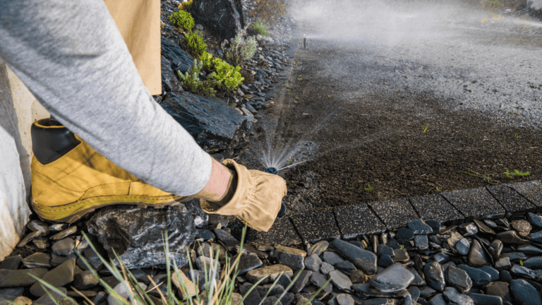 A person wearing work boots and gloves adjusts a broken sprinkler head in a garden